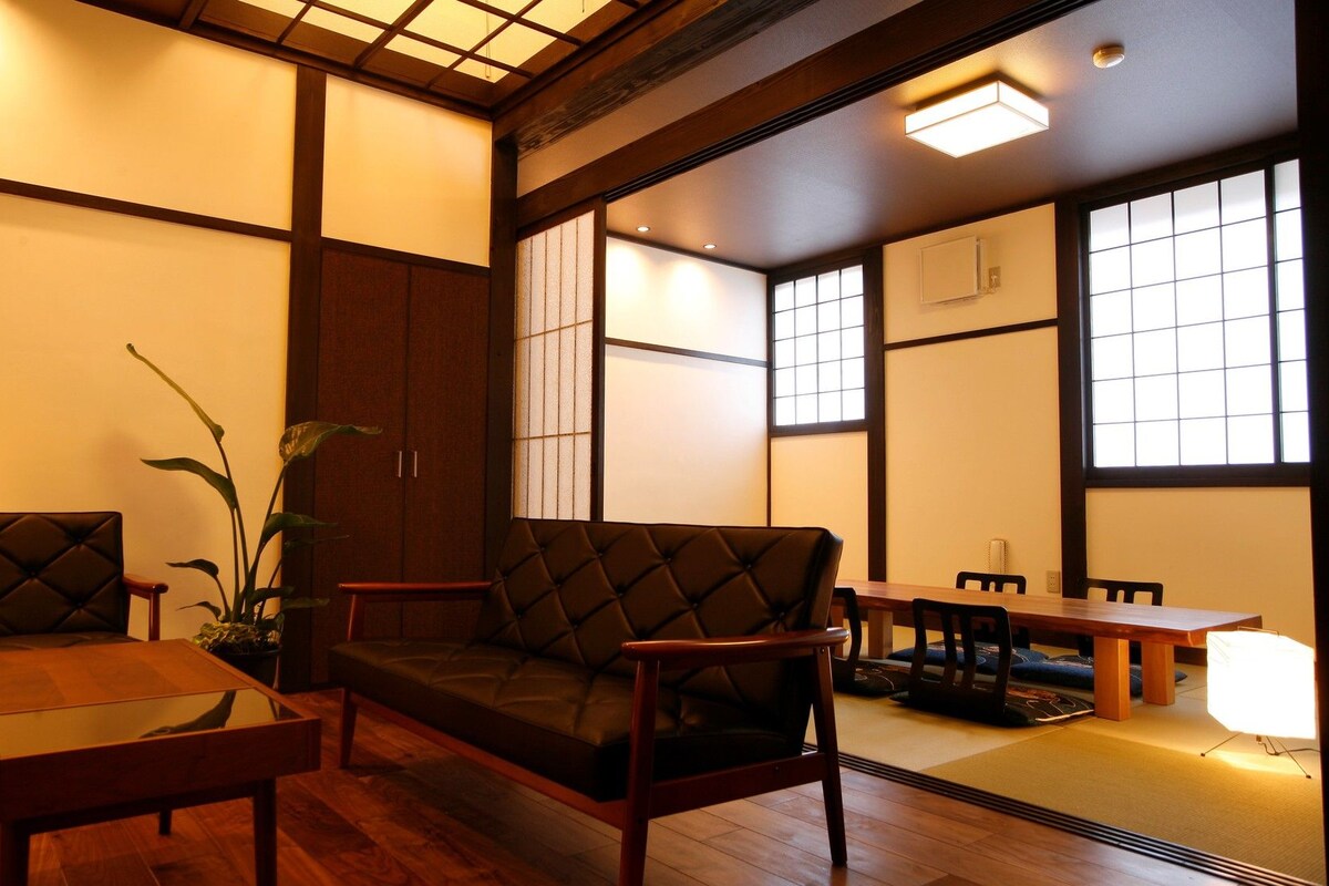 Ein traditioneller japanischer Raum mit Tatami-Böden, einem niedrigen Holztisch, einer gepolsterten Sitzbank und einer Topfpflanze.