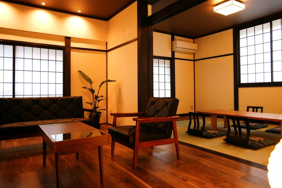 Ein traditioneller japanischer Raum mit Tatami-Boden, einem niedrigen Tisch, einer Couch und einem Sessel.