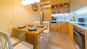 A compact kitchen with a dining area, wooden cabinets, a built-in oven, and a countertop with a coffee machine. - Anatoli Residence - in the Old Town of Rethymno (Rethymno)