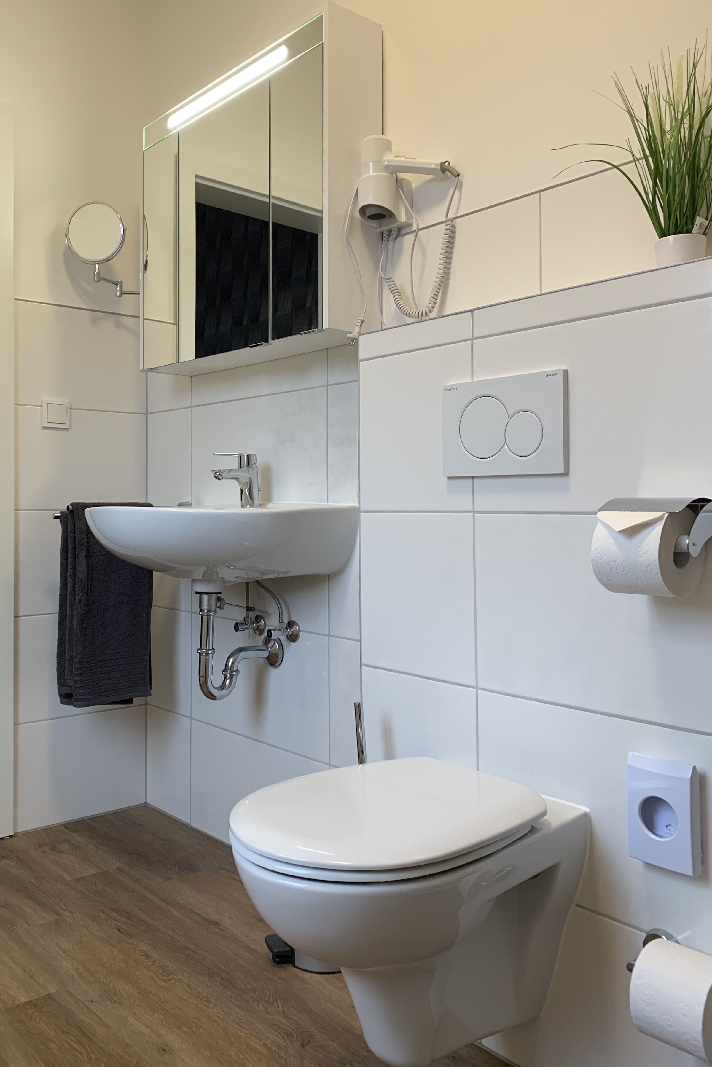 A modern bathroom with a white sink, toilet, and a mirror above the sink.