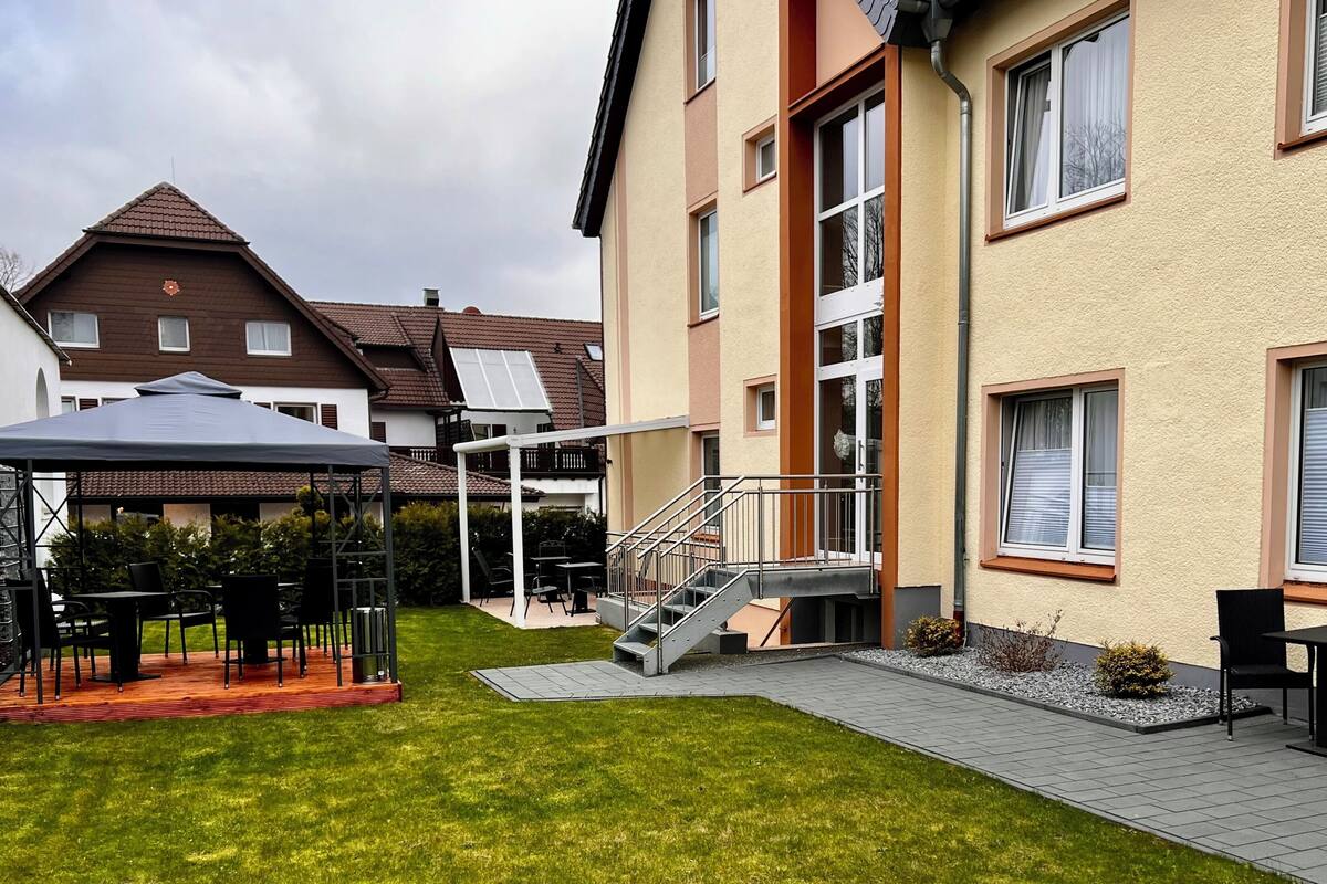Ein Wohngebäude mit überdachter Außenveranda, einer Treppe und einem kleinen Garten.