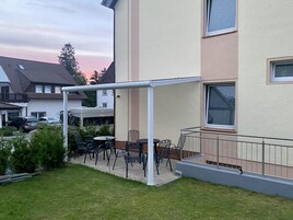 Un edificio residencial con un patio cubierto y mobiliario exterior.