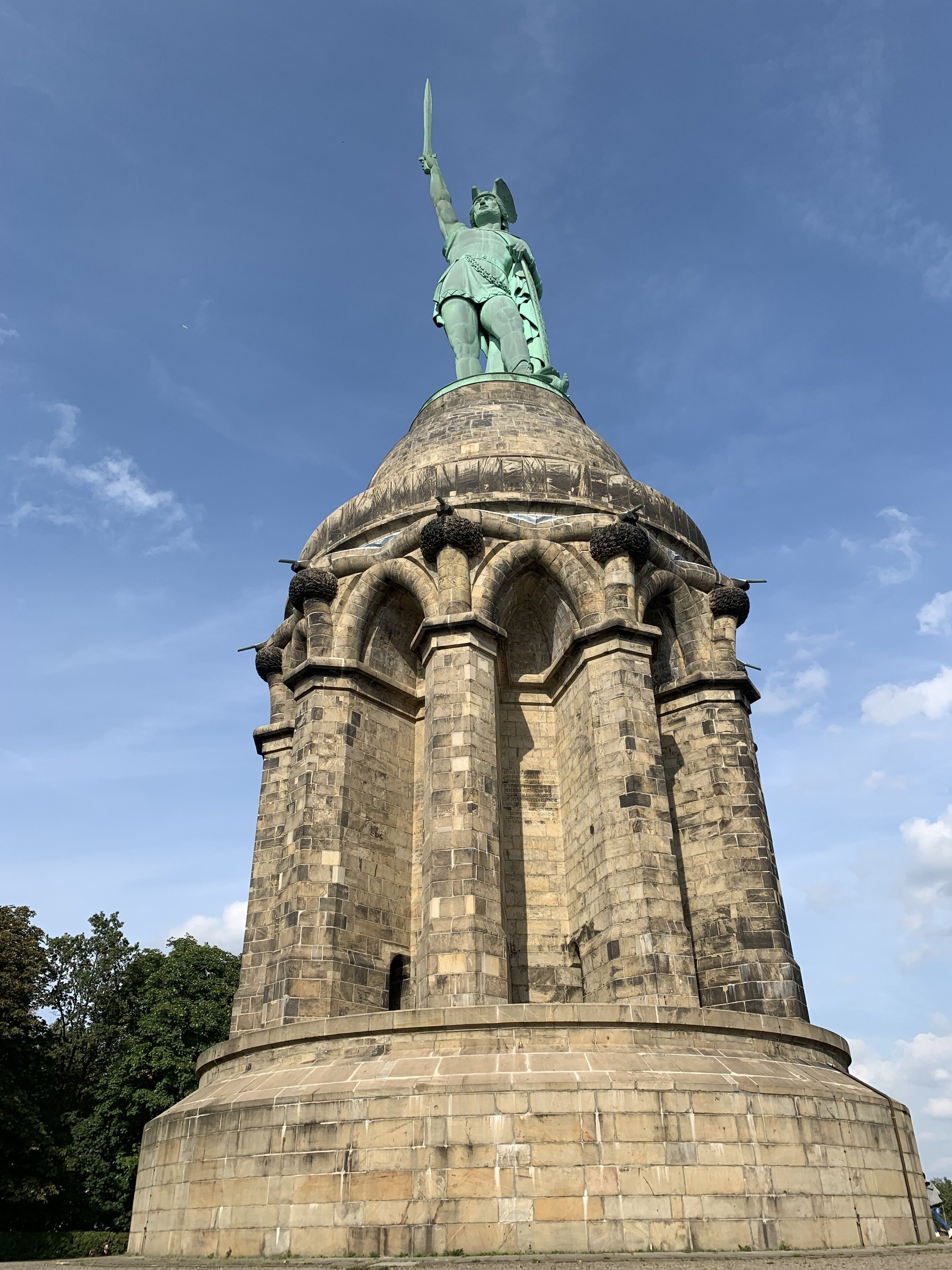 A statue atop a stone tower with a dome and arches.