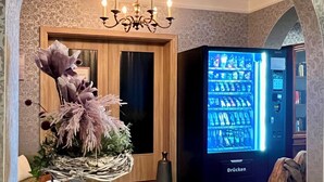 Ein Raum mit einer Chandelieber, einem Automaten, einer Holztür und einer dekorativen Vase.