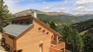 Una cabaña de madera con balcón, con montañas al fondo.