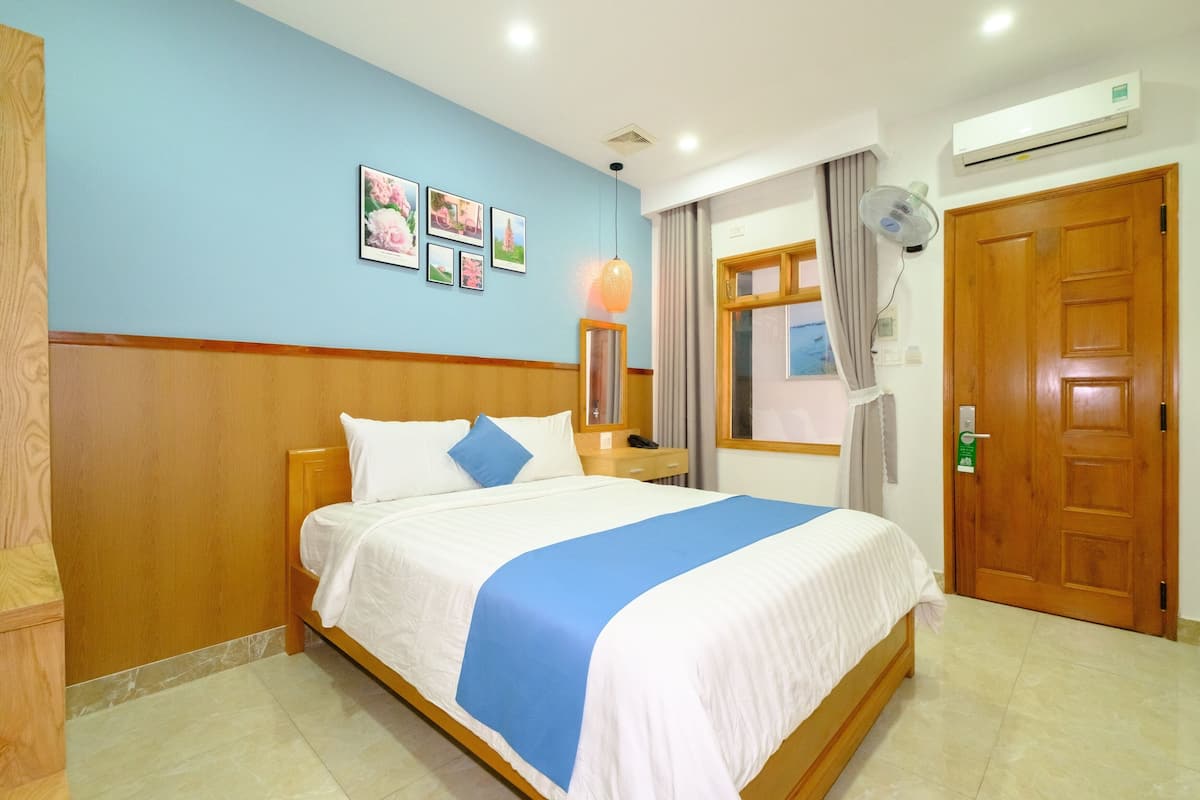 A hotel room with a bed, wooden headboard, blue walls, and a window with curtains.