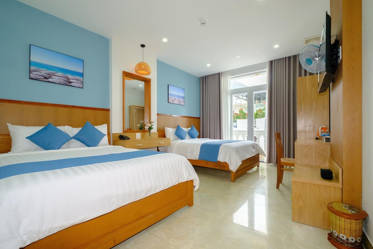 A hotel room with two beds, a wooden headboard, a TV, a fan, and a window with curtains.