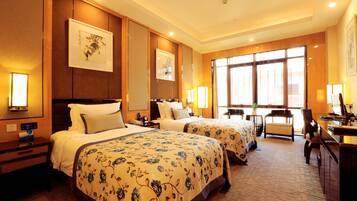 Quarto de hotel com duas camas, uma escrivaninha e uma cadeira. Grandes janelas e vista para o exterior.