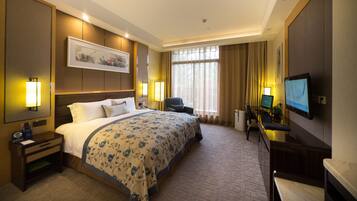 Una habitación de hotel con una cama grande, un escritorio con una computadora, una silla y un televisor.