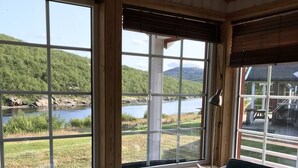 Et hyggeligt værelse med udsigt over en sø og bakker, med en grøn sofa og et lille bord med et lys.