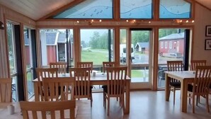 Et rummeligt område indendørs med træborde og stole, store vinduer og et højt til loftet.