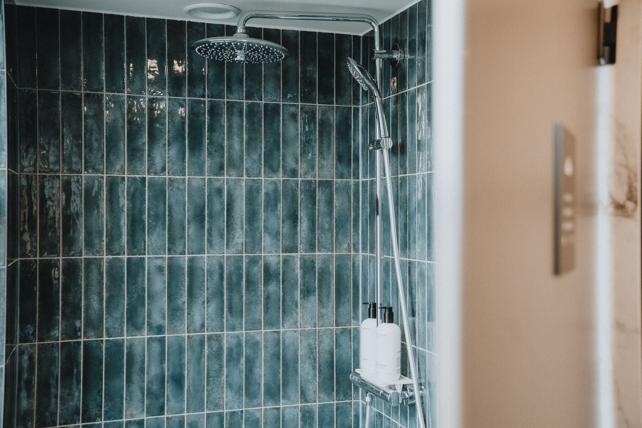 A bathroom with dark blue tiled walls, a showerhead, and a handheld shower attachment.
