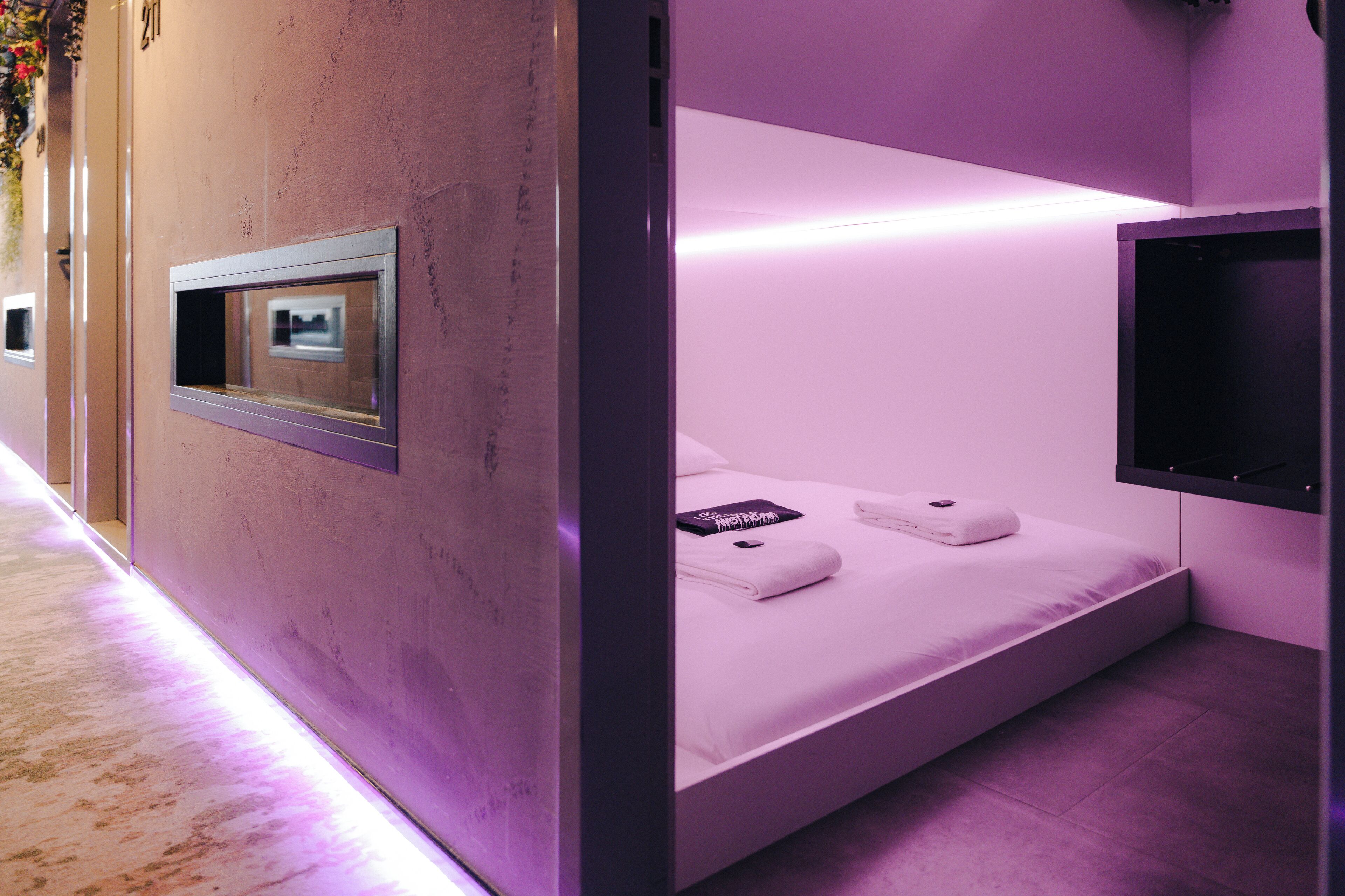 Ein modernes Zimmer mit Bett, einem Wand-Fernseher und einem kleinen Fenster.