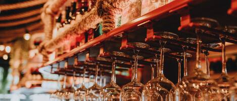 A bar with multiple wine glasses hanging from a wooden rack.
