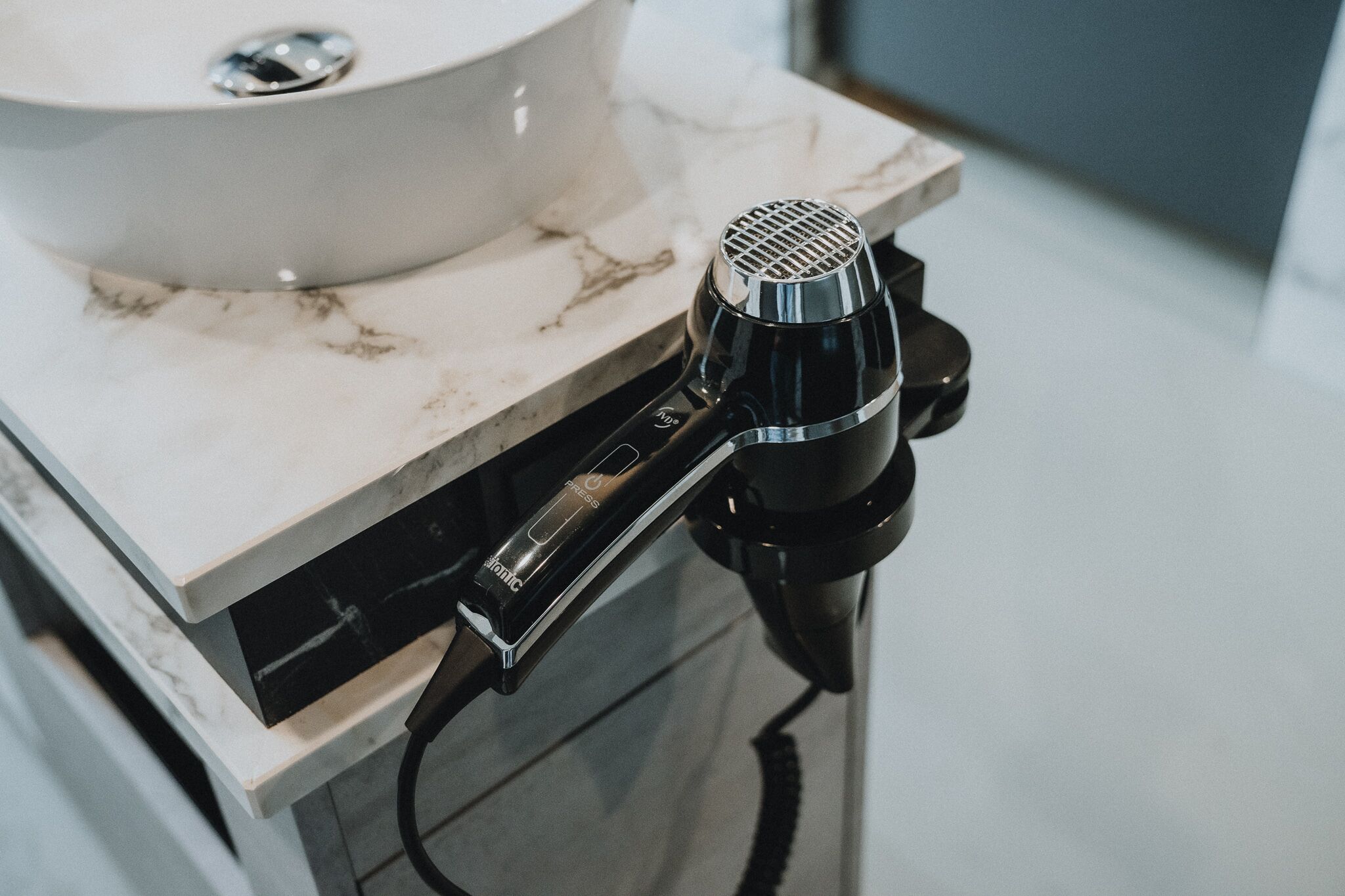 A bathroom with a white sink and a black hairdryer on a marble countertop.