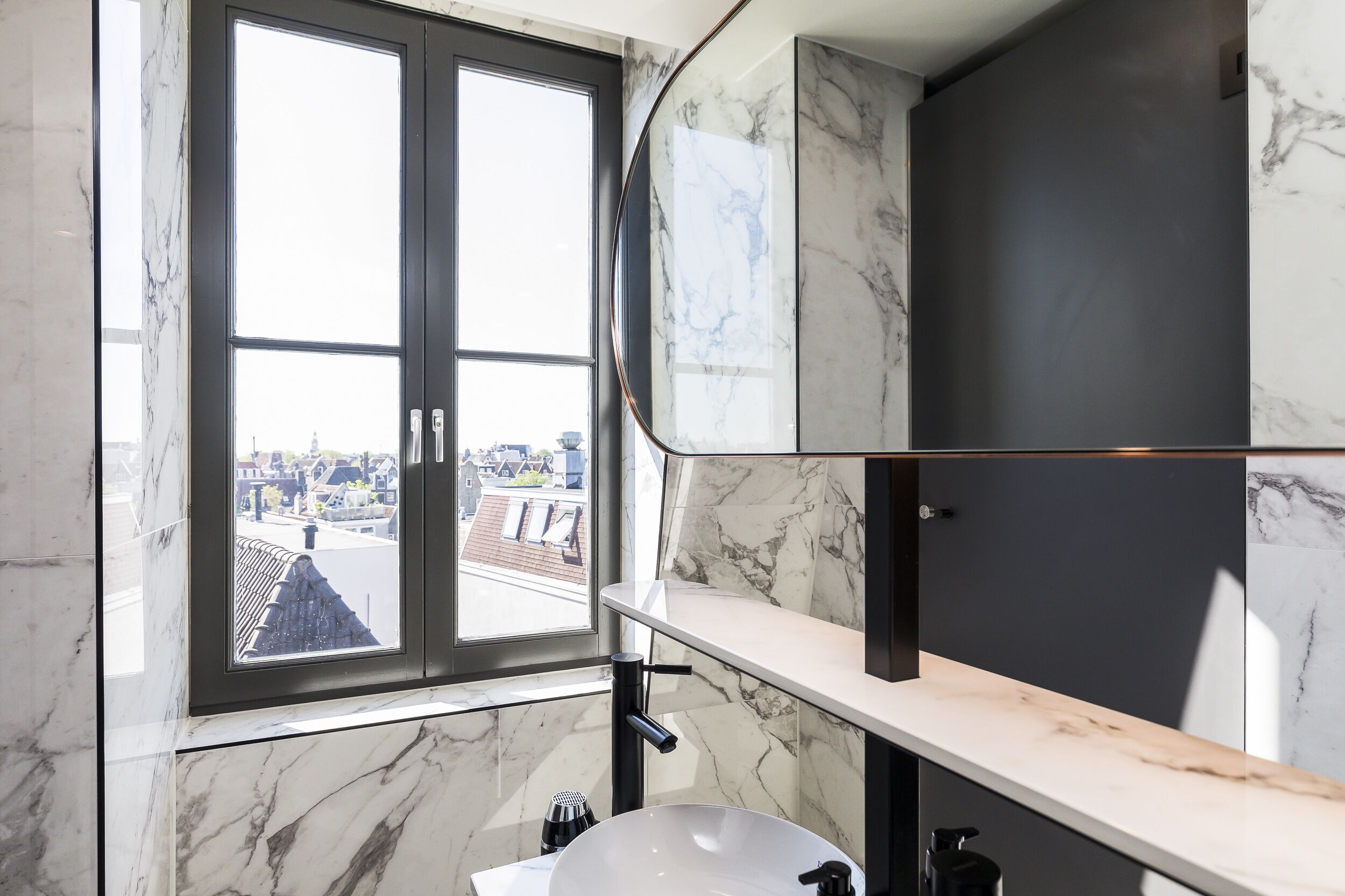 Ein Badezimmer mit großem Fenster, weißem Waschbecken und Marmorwänden.