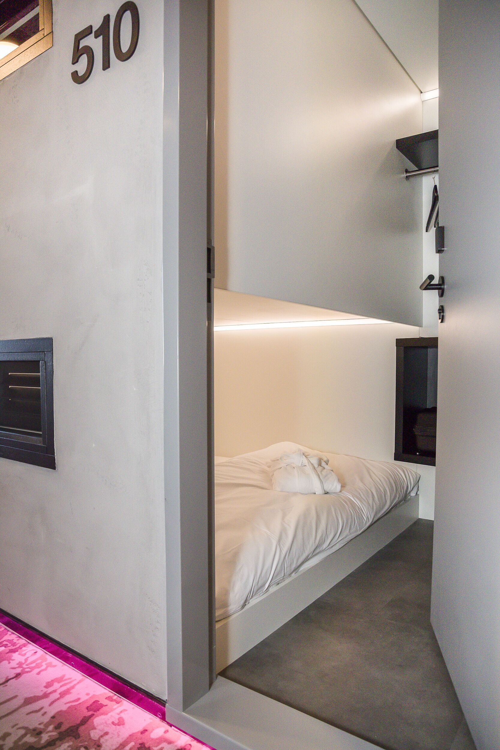 A compact, modern room with a bunk bed, a small bedside table, and a wall-mounted shelf.