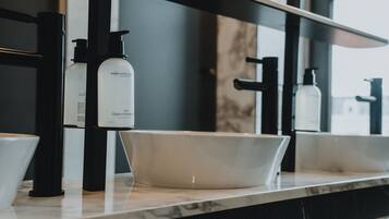 Un baño con lavamanos blanco, dispensadores de jabón negros y un espejo sobre el lavamanos.