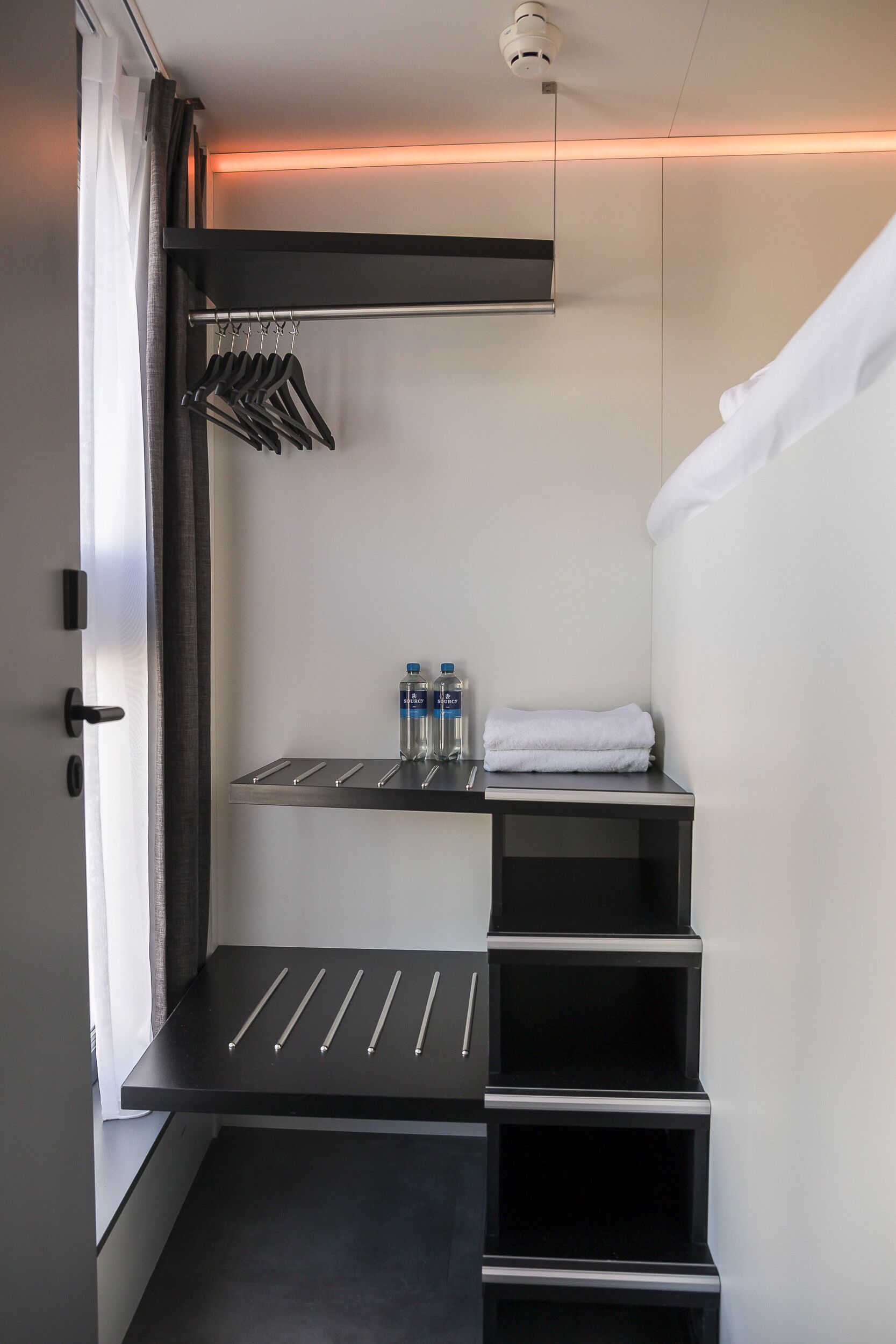 A modern bathroom with a towel rack, a shelf with bottles, and a neatly folded towel.