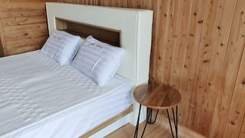 A bed with a white headboard and two pillows, a small wooden side table, and wooden panel walls.