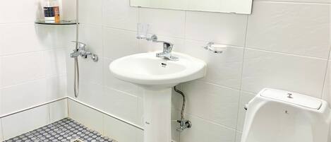 A bathroom with a white sink, a mirror, and a toilet. There is a showerhead and a soap dispenser on the wall.