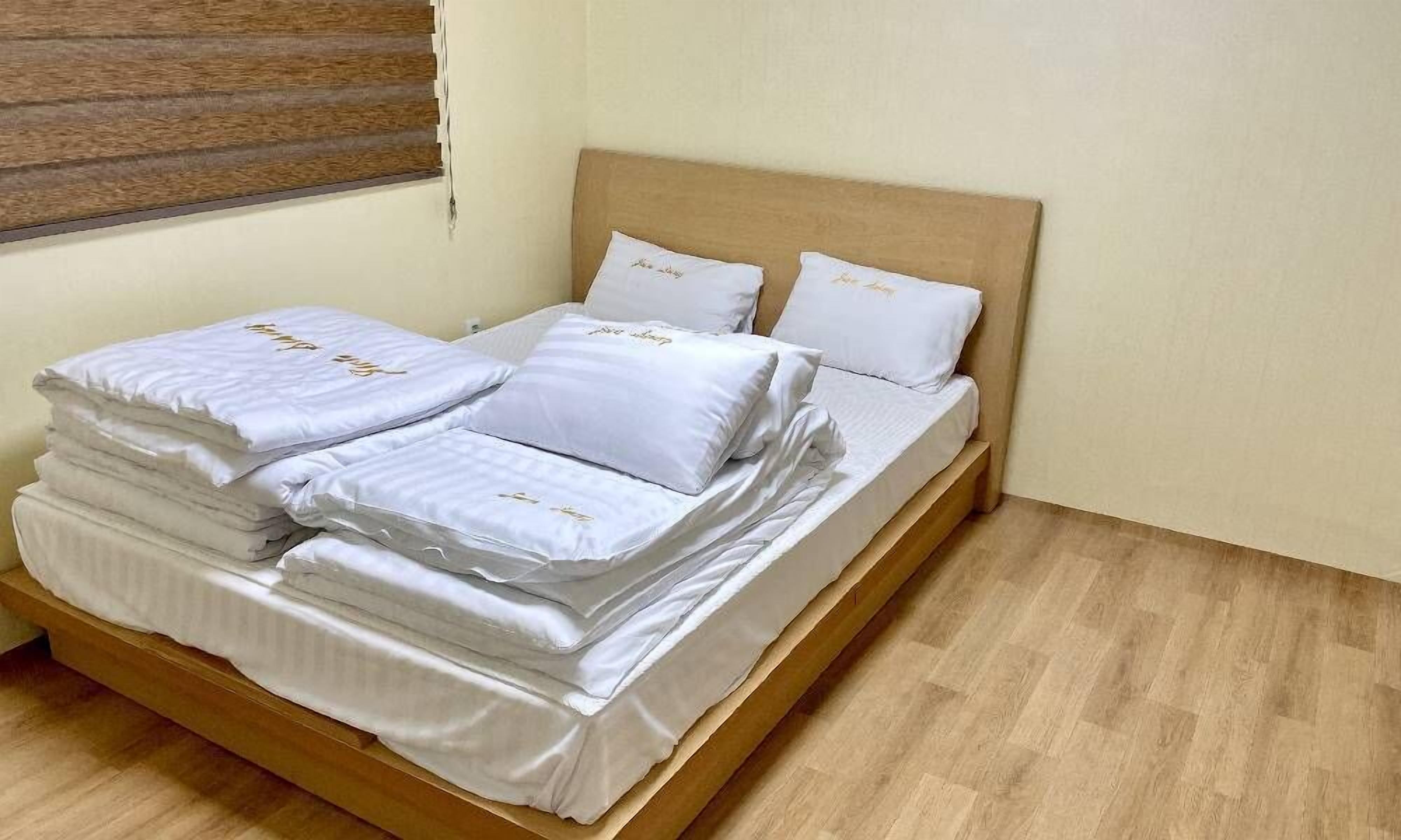 Una cama bien hecha con sábanas y almohadas blancas, un cabecero de madera y una ventana con persianas.