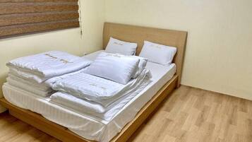 Una cama bien hecha con sábanas y almohadas blancas, un cabecero de madera y una ventana con persianas.