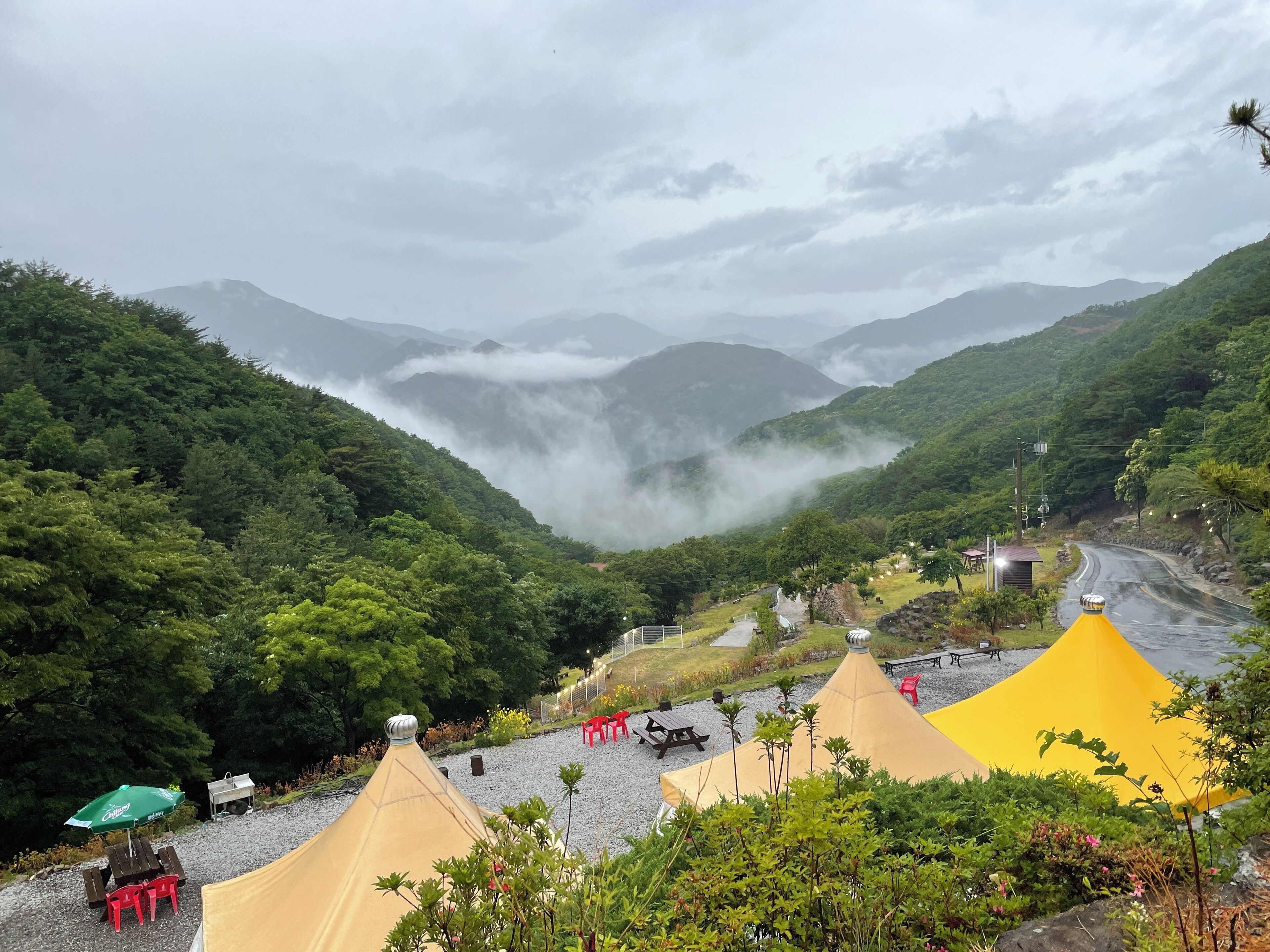 Un paysage montagneux traversé par une route sinueuse, des tentes installées pour le camping et un espace pique-nique avec des tables et des chaises.