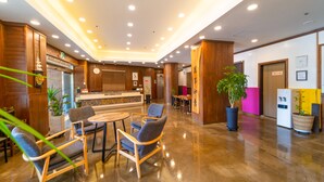 En hotellobby med träpanel, en receptionsdisk, en sittgrupp och en krukväxt.