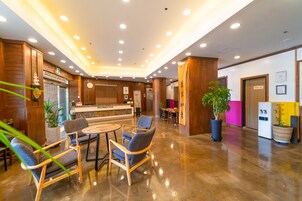 Un vestíbulo de hotel con paneles de madera, mostrador de recepción, zona de estar y una planta en maceta.