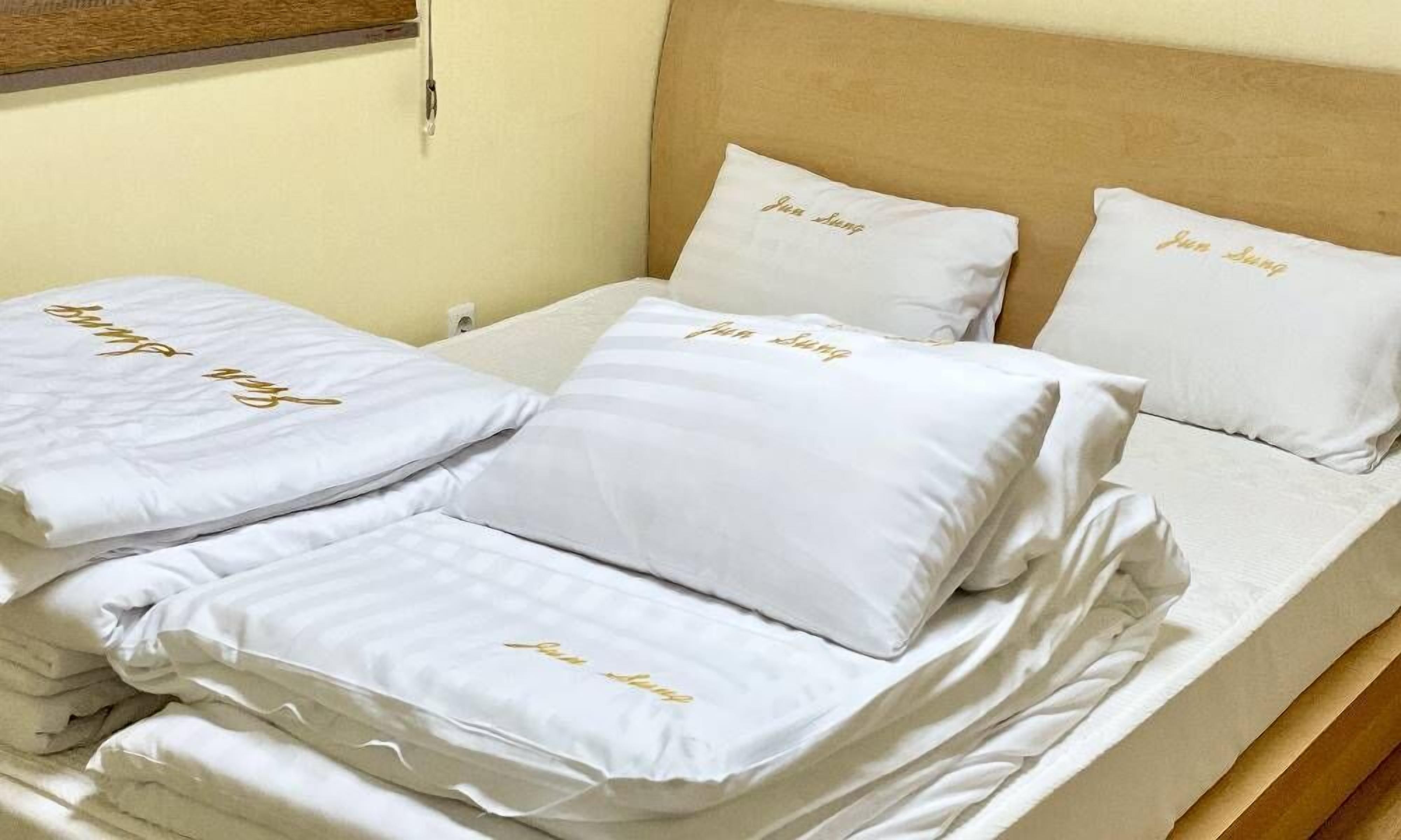 A neatly made bed with white bedding and pillows, each featuring gold lettering.