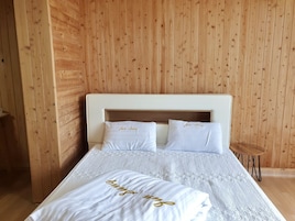 Una cama bien hecha con sábanas blancas y letras doradas, frente a una pared revestida de madera.