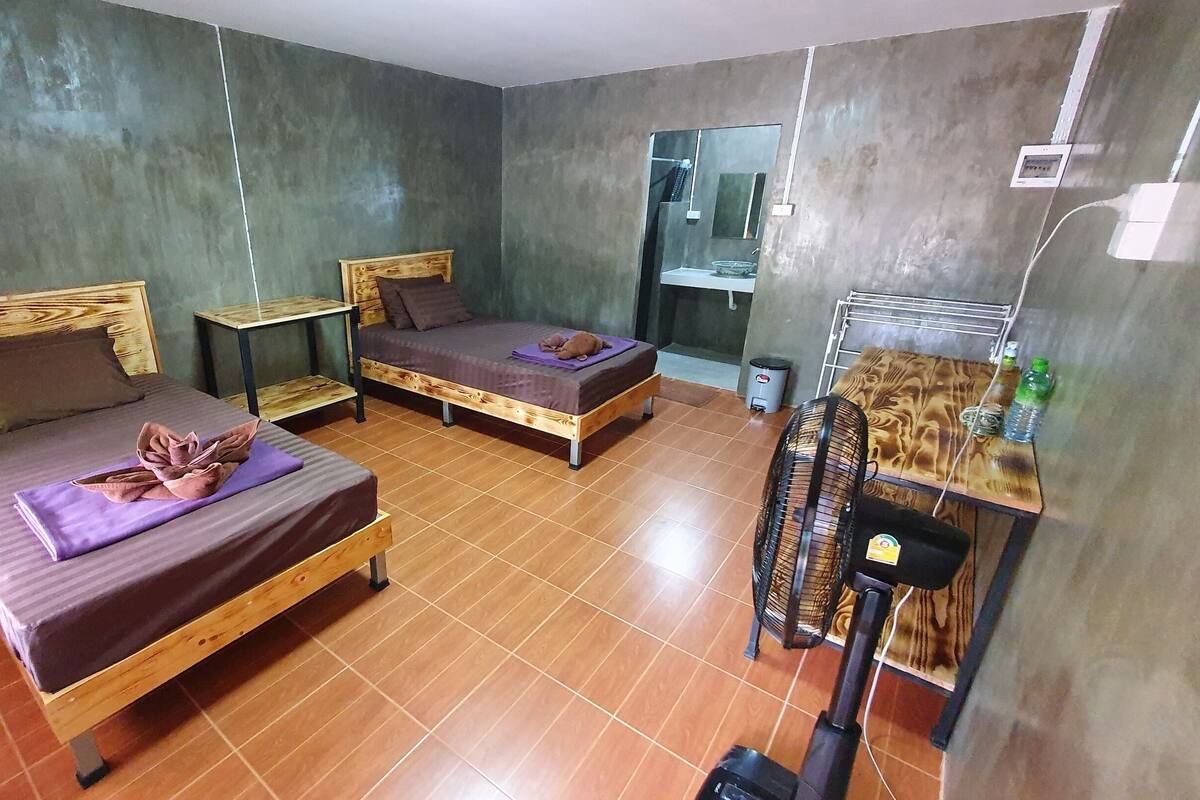 A room with two wooden beds, a small table, a mirror, and a fan.
