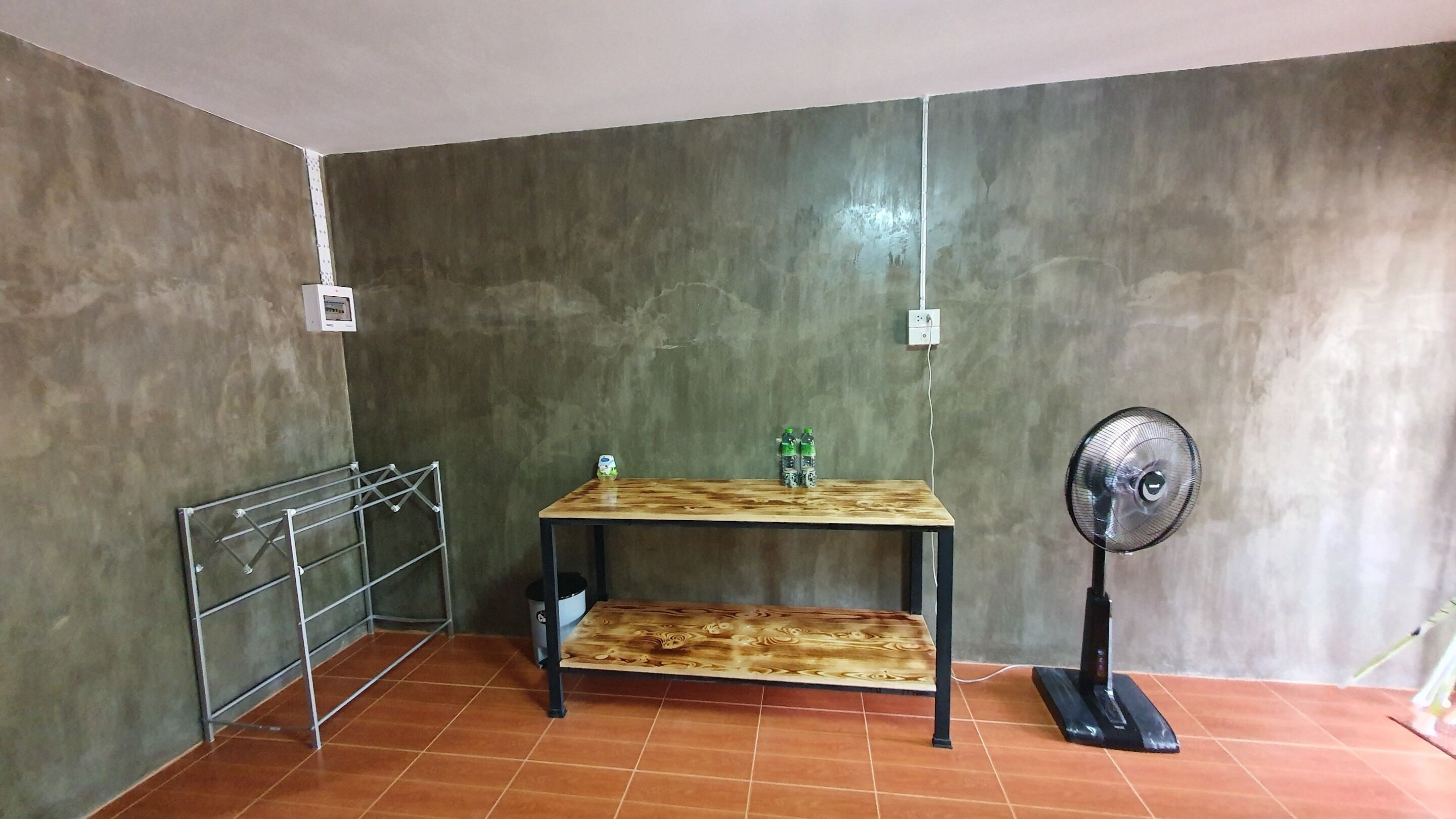 A room with a wooden table, a metal rack, a fan, and a tiled floor.