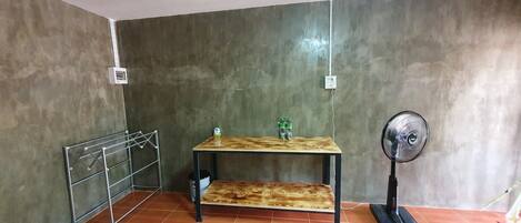 Una habitación con una mesa de madera, un perchero metálico, un ventilador y piso de baldosas.