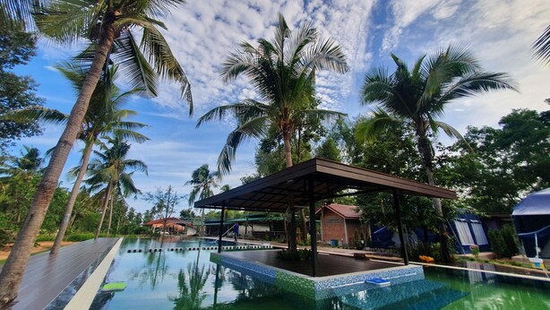 A swimming pool with a tiled edge, surrounded by palm trees and a covered pavilion. - Moonshine Resort Chumphon (Chumphon)