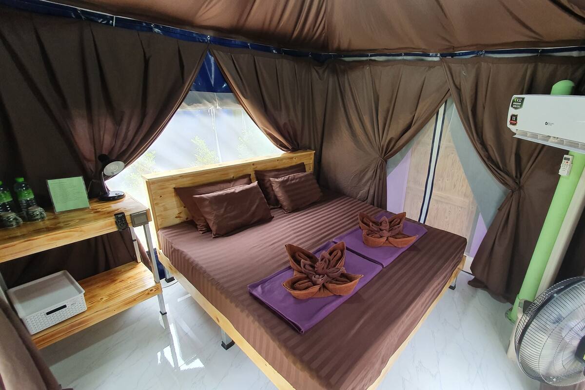 A compact, well-organized room with a bed, a desk, and a fan.