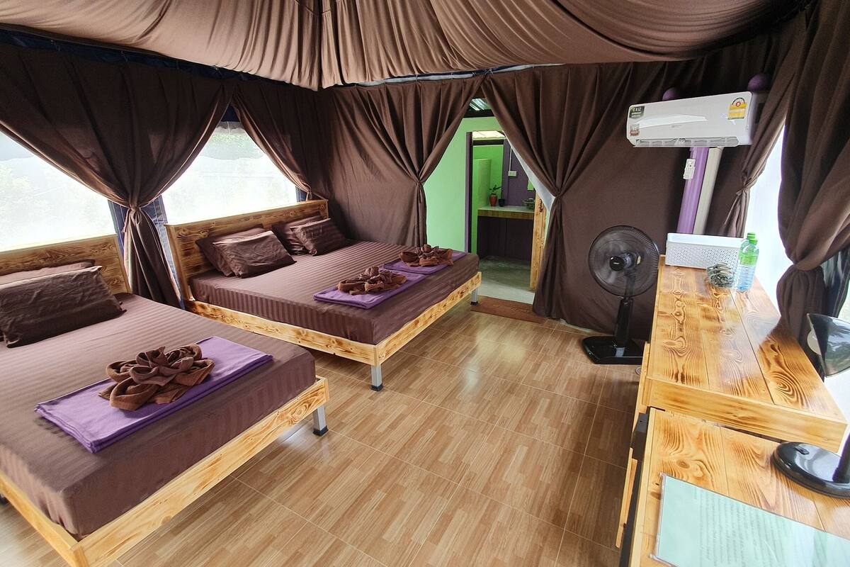 A room with two beds, a wooden desk, an air conditioner, and a fan.