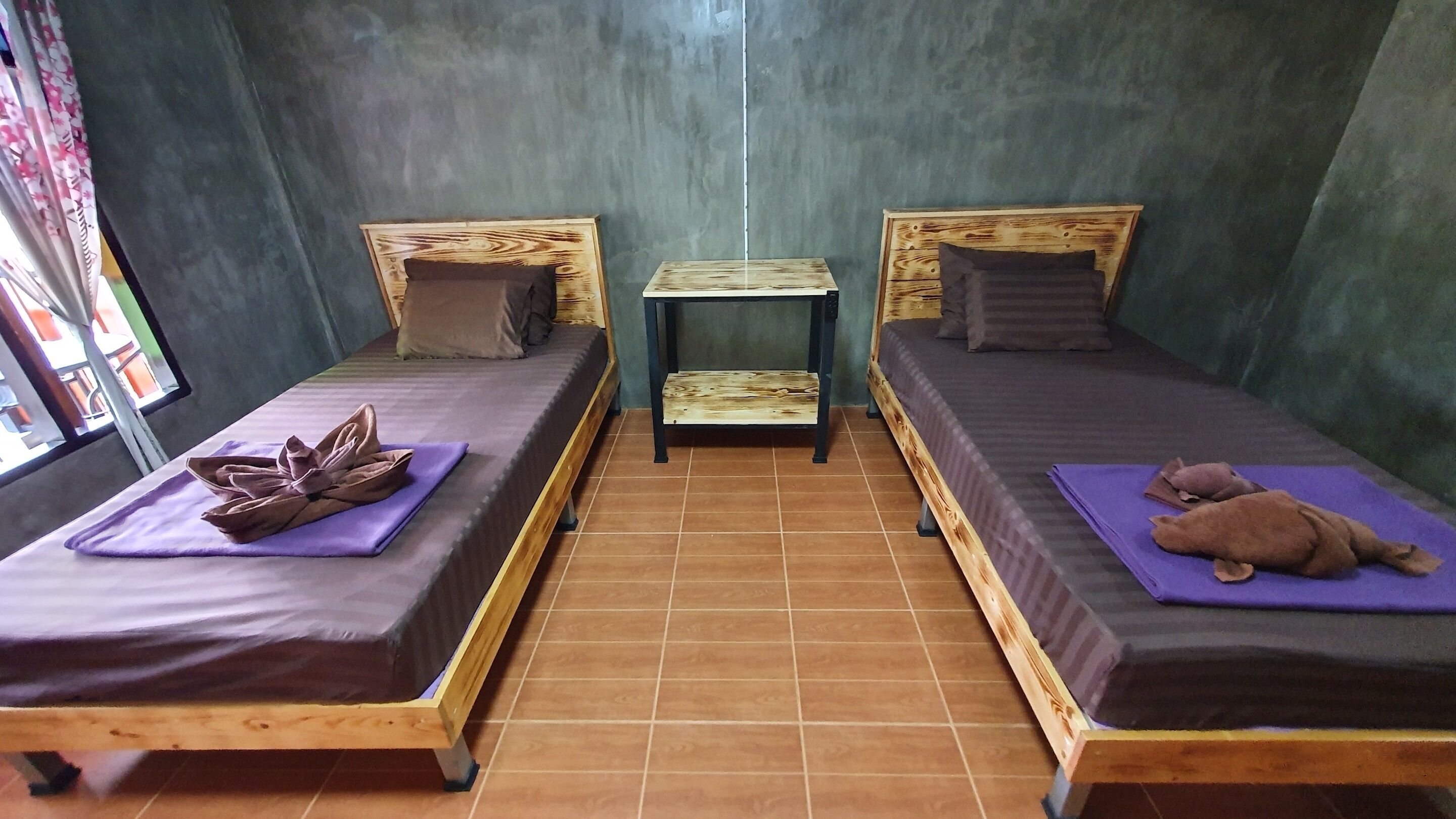 Dos camas de madera con almohadas y toallas, una mesita pequeña y una ventana con cortinas.