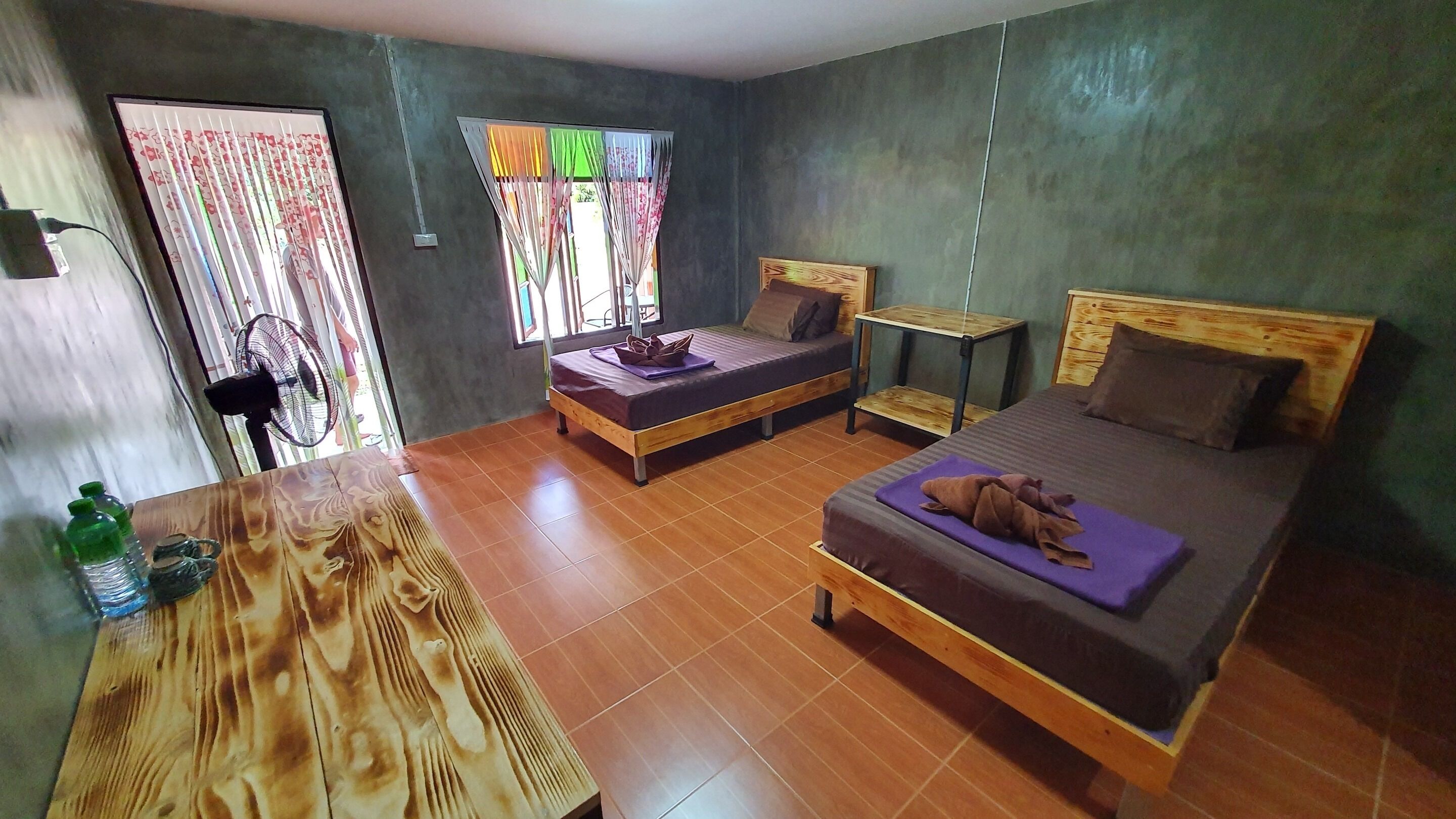 A room with two beds, a wooden table, and a window with colorful curtains.