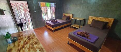 A room with two beds, a wooden table, and a window with colorful curtains.