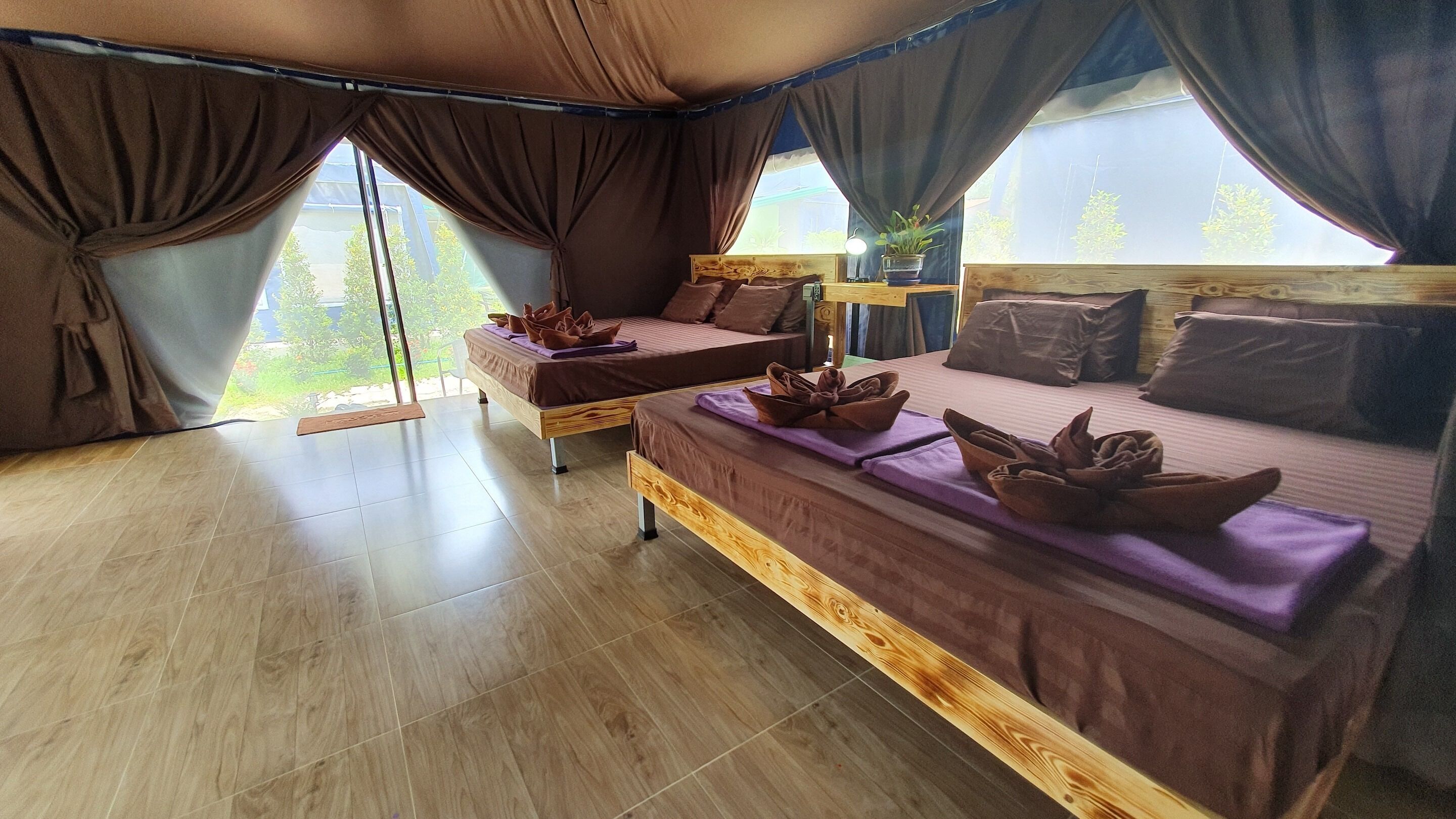 A room with two beds, large windows, and a view of greenery outside.