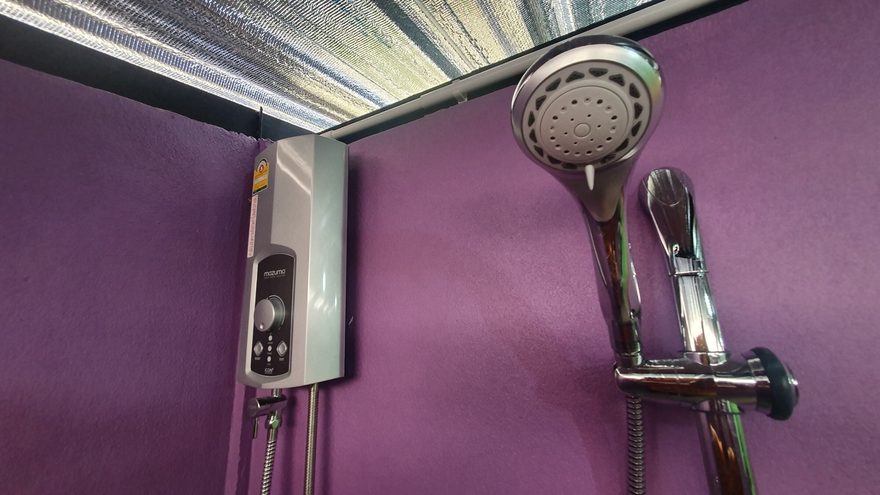 Un baño con pared morada, cabezal de ducha de mano y panel de control en la pared.