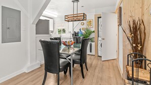 A modern kitchen with a glass dining table, black chairs, and a hanging light fixture.