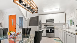 A modern kitchen with white cabinets, a stainless steel refrigerator, and a glass dining table with black chairs.