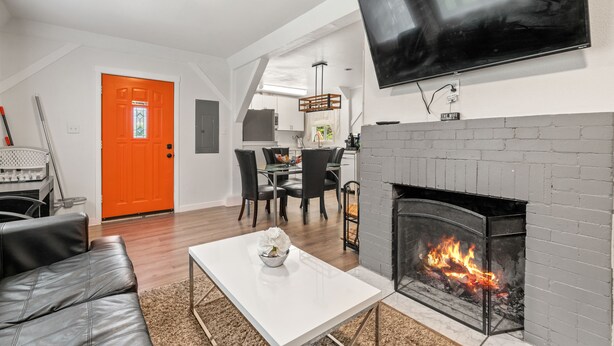 A modern living room with a fireplace, a dining area, and a bright orange door.
