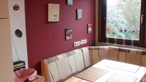 A dining area with a table, chairs, and a window with a view of trees. - Haus Tannenweg (Niestetal)