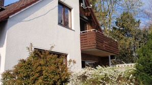 A two-story house with a balcony, surrounded by greenery. - Haus Tannenweg (Niestetal)