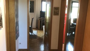 A hallway with wooden flooring, green rugs, a violin on the wall, and a mirror reflecting a room with a TV and a chair. - Haus Tannenweg (Niestetal)