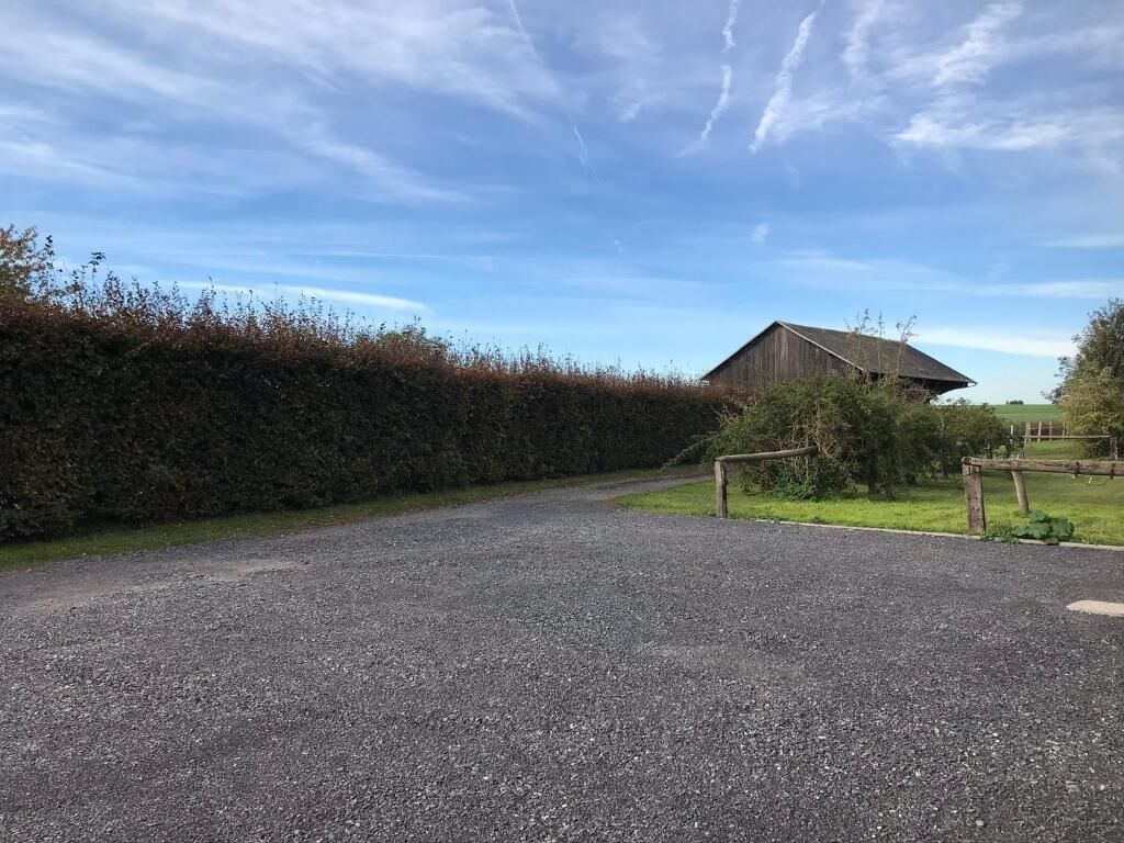 A gravel driveway leading to a wooden barn with a metal gate.